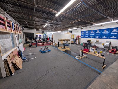 The practice field set up with wooden field elements and AprilTag targets, with a team 2363 robot on the carpet and award banners on the back wall.