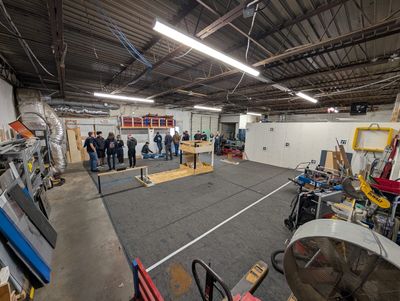 Wide view of the practice field from one corner, with groups of students and mentors near wooden field element mockups at the far end.