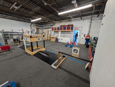 Close view of wooden field element mockups with AprilTag targets and a low black platform, with a team 2363 robot in the background.